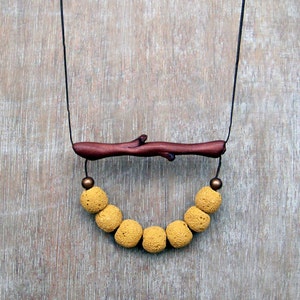 Op de afbeelding: Een ketting met een hanger van een bruine houten tak en een rij gele kralen.
