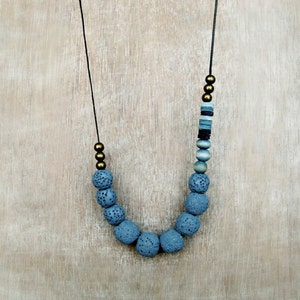 Op de afbeelding: Een ketting gemaakt van donkerblauwe lavasteen kralen en gouden kralen. De ketting is aan een zwart koord.