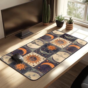 May include: Rectangular mouse pad featuring a celestial design with suns, moons, and stars in orange and cream colors on a dark blue background. The mouse pad is on a wooden desk with a computer monitor and a black mouse.