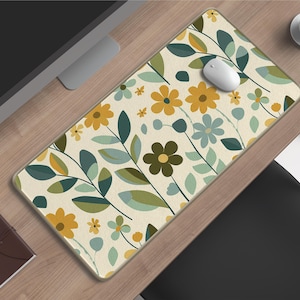 May include: A rectangular mouse mat with a floral pattern of yellow, green, and blue flowers and leaves on a cream background. A white computer mouse rests on the mat. A small brown notebook and a coffee cup are also visible.