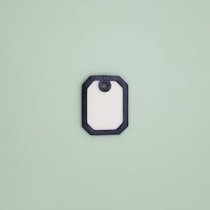 Op de afbeelding: Een blanco, rechthoekige hondenpenning met een donkerblauwe rand en een gat aan de bovenkant. De penning heeft een wit midden en staat tegen een lichtgroene achtergrond. De vorm van de penning is een afgeronde rechthoek.