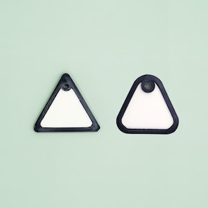 May include: Two triangular-shaped, white objects with a black border and a hole at the top. The objects are set against a light green background. The objects appear to be tags or labels.