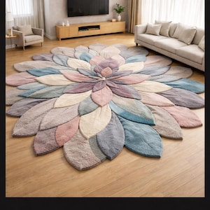May include: A large, floral-shaped area rug in a living room setting. The rug features petal-like shapes in shades of pink, purple, blue, and beige. The rug is placed on a hardwood floor, with a sofa and entertainment center in the background.