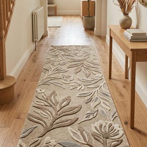 Può includere: Un lungo tappeto rettangolare da corridoio caratterizzato da un motivo botanico trapuntato in rilievo nei toni del beige, tortora e crema. Il design è composto da foglie stilizzate e motivi floreali che creano una superficie tridimensionale.