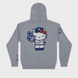 Op de afbeelding: Grijze hoodie met een Hello Kitty-afbeelding met een Dodgers-baseballpet en een foam finger. De hoodie heeft een capuchon en lange mouwen. Het Dodgers-logo is zichtbaar.