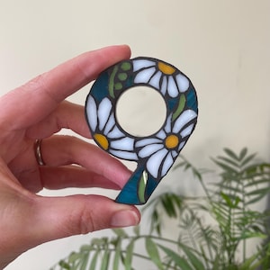 May include: A mosaic number nine made of white and yellow glass tiles, shaped like daisies, with a teal green background.
