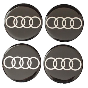 Puede incluir: Cuatro emblemas circulares negros para coche con el logotipo de Audi en blanco. El logotipo consta de cuatro anillos entrelazados. Los emblemas tienen un acabado brillante y están dispuestos en forma cuadrada.