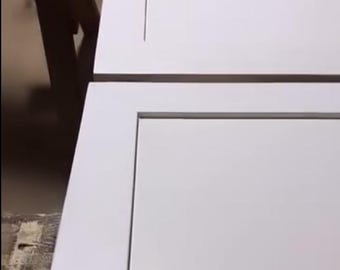 Può includere: Due ante di armadi bianche con un design a pannello incassato. Le ante sono rettangolari con un'estetica pulita e moderna. L'immagine è ripresa da un'angolazione che mostra la parte superiore e laterale delle ante. Le ante sembrano appena verniciate.