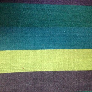 May include: A close-up of a striped fabric with alternating bands of dark teal, light teal, light green, and dark gray.
