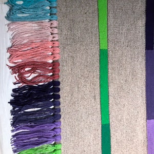 Puede incluir: Una alfombra tejida con un borde de flecos en varios colores, incluyendo azul, rosa, rojo, morado y verde. La alfombra tiene una franja verde en el centro y una franja morada en el lado derecho.