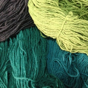 May include: A collection of yarn in shades of green, teal, and black. The yarn is arranged in a pile, with the green yarn on top.