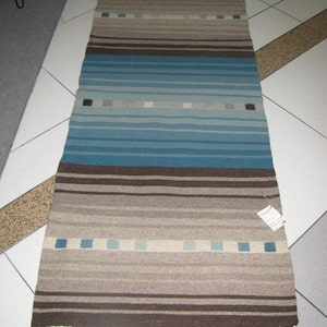 May include: A long, rectangular rug with brown, blue, and beige stripes. The rug has a fringe on both ends.