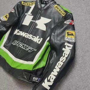 May include: Black and green Kawasaki motorcycle jacket with white accents. Features the Kawasaki logo, Dunlop and Rocket branding, and Agip patch. The jacket has a zip closure and is made of leather.
