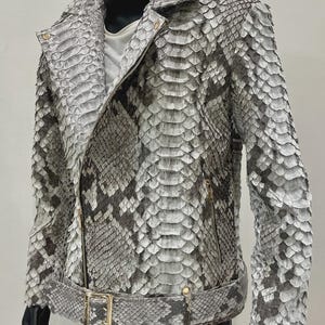 May include: A grey and white snakeskin-patterned leather jacket with a zip closure, belt, and gold-coloured hardware. The jacket has a classic biker style with a notched collar and long sleeves.