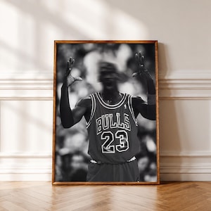 May include: A black and white framed wall art print featuring a basketball player in a Chicago Bulls jersey with the number 23. The player has both arms raised in a celebratory gesture, with a motion blur effect on the head and upper body.