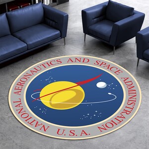 以下が含まれることがあります： NASAのロゴが入った丸いラグ。デザインは、赤い弧のある黄色い惑星、白い球体、そして「NATIONAL AERONAUTICS AND SPACE ADMINISTRATION U.S.A.」というテキストが青い中心部の周りを円形に配置されています。