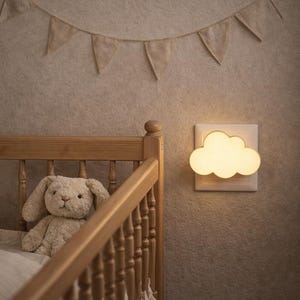 Peut inclure: Un lit bébé en bois avec un lapin en peluche et une veilleuse en forme de nuage. Une guirlande beige avec des fanions triangulaires est suspendue au-dessus du lit. La pièce a une palette de couleurs neutres.