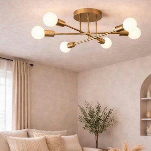 May include: A gold-coloured ceiling light fitting with six spherical bulbs. The fixture has a circular base and radiating arms. The bulbs are a warm white, and the fitting is mounted on a white ceiling. The room has a neutral colour palette.