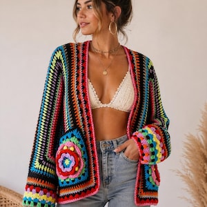 May include: A vibrant, open-front crochet cardigan in a patchwork design. The colorful garment features a mix of rainbow hues, including red, orange, yellow, green, blue, and purple, with black accents. The cardigan has long sleeves and a unique floral motif.