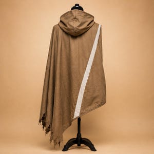 May include: A brown hooded cloak with a white stripe down the back, displayed on a black mannequin. The cloak has a unique, tattered edge design. The cloak is made of a soft, draping fabric.