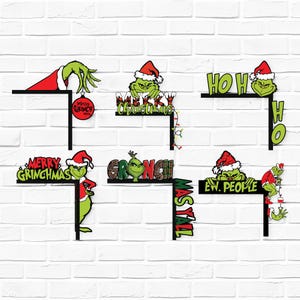 May include: A set of six black L-shaped corner decorations featuring green characters in red Santa hats. Designs include text such as Merry Christmas, Ho Ho Ho, Merry Grinchmas, Grinch, Mas Y'all, and Ew. People, along with festive ornaments and lights.