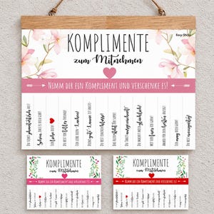 Può includere: Un grande cartello da parete e due cartoline più piccole con il testo KOMPLIMENTE zum Mitnehmen, un cuore rosa e decorazioni floreali. I cartelli includono una striscia orizzontale rosa con il testo Nimm dir ein Kompliment und verschenke es, seguita da strisce verticali staccabili con varie frasi in tedesco.