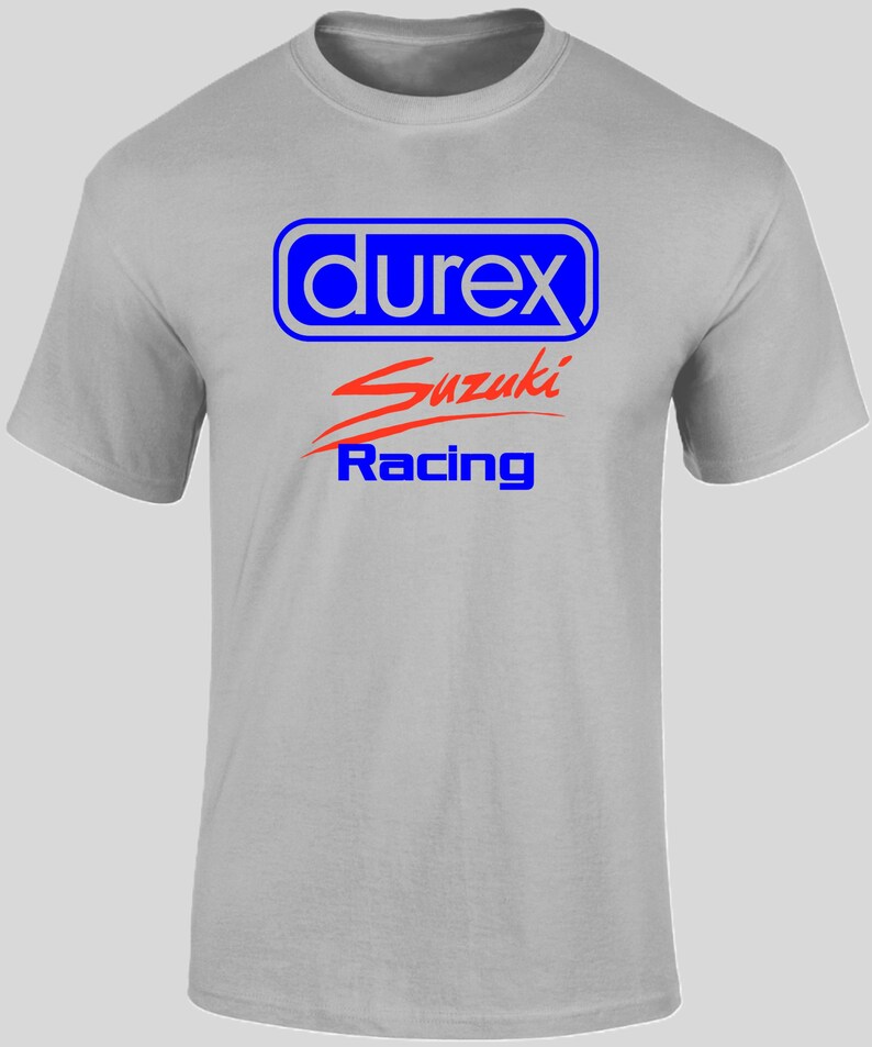May include: A light gray t-shirt featuring the text "durex" in a blue and white rectangular design, with "Suzuki" in red script and "Racing" in blue below. The shirt has short sleeves and a crew neck.