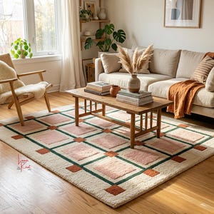 May include: A rectangular area rug featuring a cream-colored base with a grid pattern of dark green lines, light pink squares, and small burnt orange squares at the intersections. The rug has a textured pile and includes a small red logo in the corner.