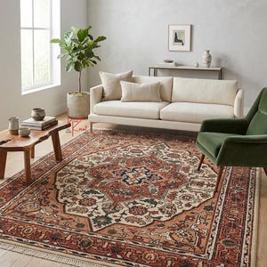 May include: A rectangular area rug featuring a central medallion pattern in shades of rust, cream, navy blue, and sage green. The rug has a detailed floral border and short white fringe along the edges, placed on a light-colored wooden floor.