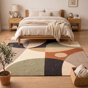 May include: A rectangular area rug featuring a geometric pattern of overlapping circles and arcs in muted tones of sage green, terracotta, charcoal gray, beige, and cream. The rug is positioned on a light wood floor in a bedroom setting.