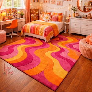 May include: A rectangular area rug featuring a repeating wavy pattern in vibrant shades of hot pink, orange, and yellow. The rug has a thick, tufted texture and covers a portion of a wooden floor. The logo Loom and Knot Shop is visible in the corner.