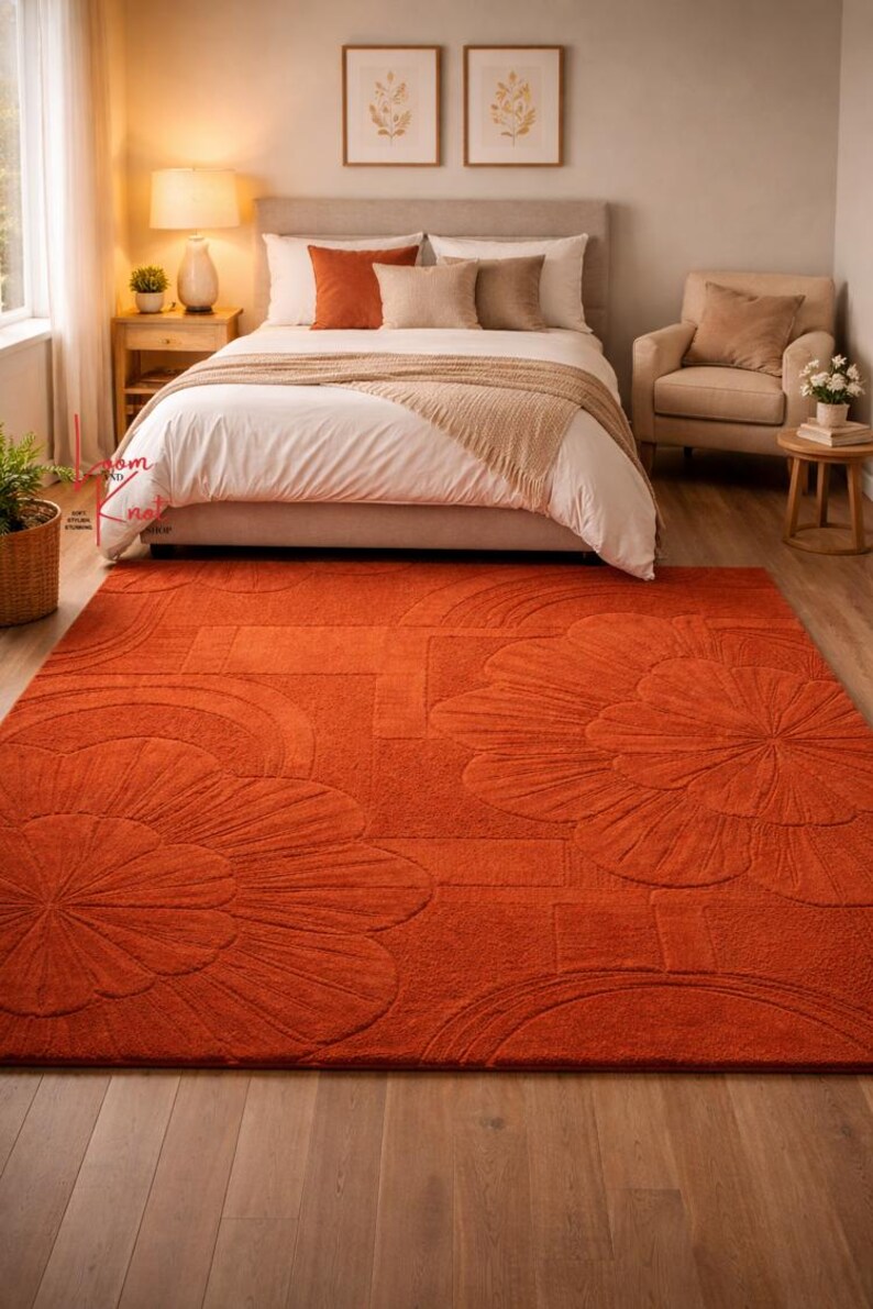 May include: A rectangular area rug in a solid burnt orange color featuring a raised, tufted floral and geometric pattern. The rug has a thick, textured pile with large, stylized flower motifs and curved lines embossed across the surface.