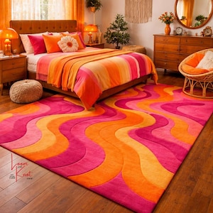 May include: A rectangular area rug featuring a vibrant, wavy pattern in shades of hot pink, bright orange, and soft yellow. The rug has a textured, carved pile design and includes a small logo in the corner that reads Loom and Knot Shop.