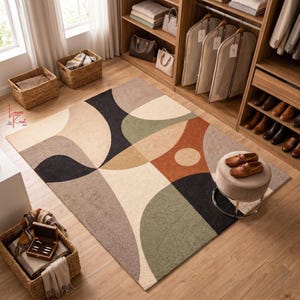 May include: A rectangular area rug featuring a geometric pattern of overlapping circles and arcs in shades of cream, charcoal, sage green, tan, and terracotta. The rug is placed on a light wood floor in a room with a wooden closet and woven baskets.