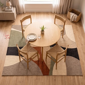 May include: A round light wood dining table with four matching chairs featuring woven seats, positioned on a large rectangular area rug with an abstract pattern of beige, brown, green, and black shapes, with a small potted plant and plate.