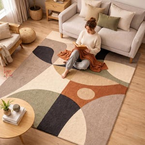 May include: A rectangular area rug featuring a geometric pattern with large, curved shapes in shades of black, sage green, terracotta, beige, and taupe. The rug has a textured, tufted surface and is laid out on a light-colored wooden floor.