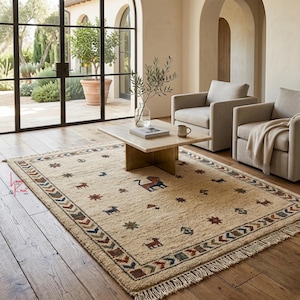 May include: Beige rectangular area rug with a patterned border and scattered animal and star motifs. The rug features a fringed edge and is placed on a hardwood floor. A central design depicts a lion-like figure.