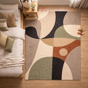May include: A rectangular area rug featuring a large-scale abstract pattern with curved shapes and geometric sections in shades of cream, beige, sage green, charcoal black, and terracotta orange, with a small circular accent in the orange section.