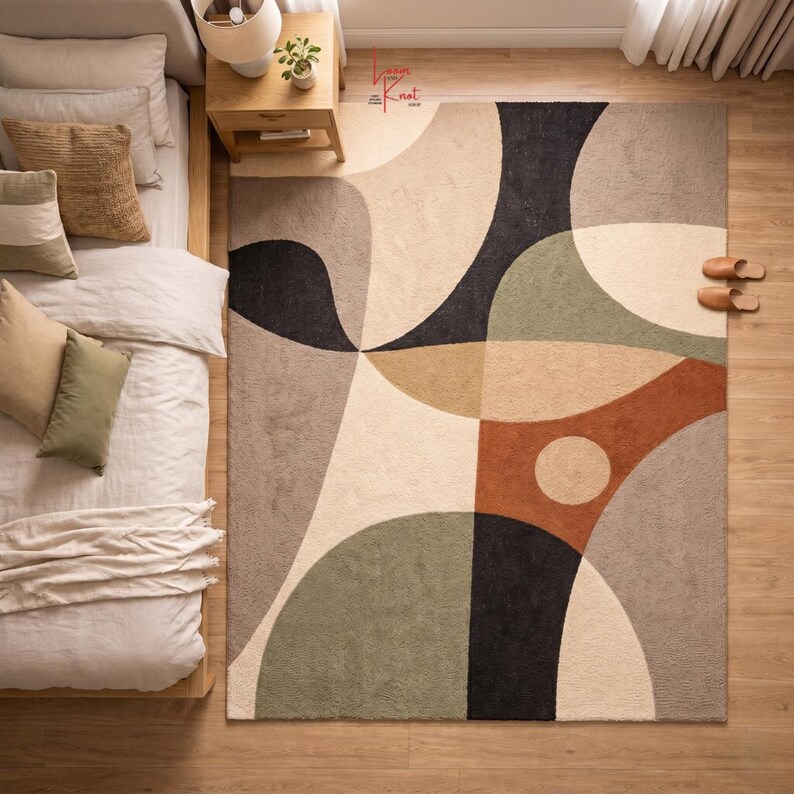 May include: A rectangular area rug featuring a large-scale abstract pattern with curved shapes and geometric sections in shades of cream, beige, sage green, charcoal black, and terracotta orange, with a small circular accent in the orange section.