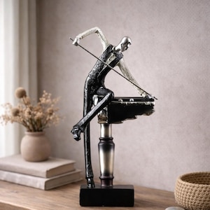 Könnte beinhalten: Dekorative Figur einer Person, die Billard spielt. Die Figur trägt eine schwarze Weste und Hose mit silbernem Kopf und Armen. Der Billardtisch ist schwarz und der Queue wird in den Händen der Figur gehalten. Die Figur steht auf einem schwarzen Sockel.