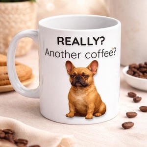 Peut inclure: Mug en céramique blanche avec l'inscription "REALLY? Another coffee?" et une illustration d'un bouledogue français marron. La tasse a une anse incurvée. Des grains de café sont visibles.