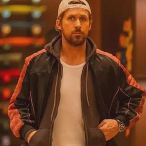 May include: A black and red jacket with a white t-shirt and a beige baseball cap. The jacket has red accents on the shoulders and sleeves. The person is wearing a watch. The background is blurred.