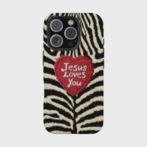 K&ouml;nnte beinhalten: Eine Handyh&uuml;lle mit Zebramuster und einem herzf&ouml;rmigen roten Aufn&auml;her. Der Aufn&auml;her hat den gestickten Text "Jesus Loves You" in Wei&szlig;. Die H&uuml;lle hat ein schwarzes Kameramodul.