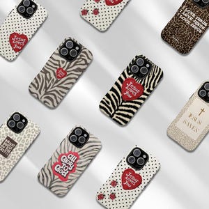 K&ouml;nnte beinhalten: Eine Sammlung von Handyh&uuml;llen mit verschiedenen Designs. Einige H&uuml;llen zeigen Zebrastreifen, Leopardenmuster und Tupfen. Mehrere H&uuml;llen haben den Text "Jesus Loves You" auf einem roten Herzen. Andere H&uuml;llen haben den Text "All Glory to God" und "Jesus Saves".
