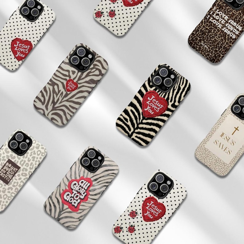 K&ouml;nnte beinhalten: Eine Sammlung von Handyh&uuml;llen mit verschiedenen Designs. Einige H&uuml;llen zeigen Zebrastreifen, Leopardenmuster und Tupfen. Mehrere H&uuml;llen haben den Text "Jesus Loves You" auf einem roten Herzen. Andere H&uuml;llen haben den Text "All Glory to God" und "Jesus Saves".