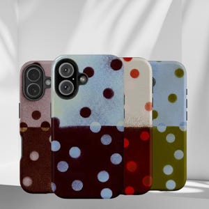May include: Four phone cases with a two-tone design. The top half of each case is a light color, while the bottom half is a darker color. Each case has a pattern of white or colored polka dots. The cases have camera cutouts.