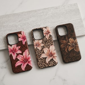 May include: Three phone cases with floral designs. One case has pink lilies on a brown background, another has pink lilies on a leopard print, and the third has brown lilies on a brown background. The cases are made of a hard material.