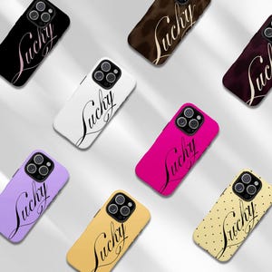 May include: A collection of phone cases in various colors, including black, white, pink, yellow, and purple. Each case features the word "Lucky" in a cursive font. Some cases have a solid color, while others have a dotted pattern.
