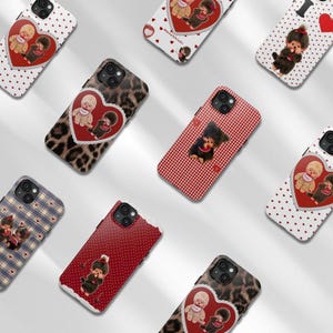 May include: A collection of phone cases with various designs. Some cases feature a heart-shaped graphic with two doll-like figures. Other cases have patterns like leopard print, red gingham, and polka dots. The cases are in different colors, including red, white, and blue.