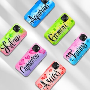May include: Six smartphone cases featuring zodiac signs in black cursive script. Designs include Aquarius on blue clouds, Gemini on green stars, Libra on pink and green stars, Capricorn on purple hearts, Taurus on blue stars, and Aries on pink hearts.